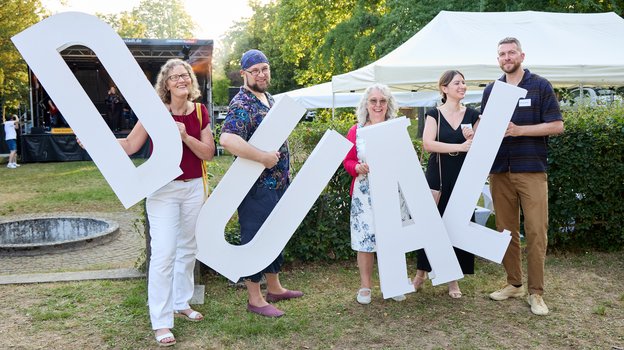Frau Wolf mit Mitarbeitenden die die Buchstaben D U A L halten