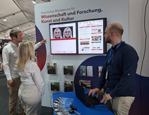 Das Team der h_da auf dem Hessentag vor einem Bildschirm mit Alterungssimulation