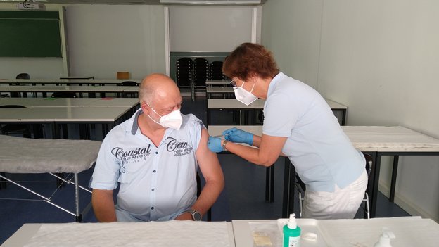 Prof. Dr. Arnd Steinmetz wird von einer MItarbeiterin des h_da-Betriebsarztes geimpft. das Foto zeigt den Moment des "Einstichs". 